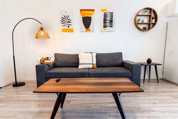 A modern living room with a grey sofa, a wooden coffee table, a floor lamp, and abstract wall art. - Africa/2Bdr/Plateau/St-Laurent/SelfCheck-In/AC/TV (Montréal)