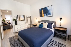 A modern bedroom with a large bed, bedside tables, a dresser, and a painting on the wall. - Blue&Gold/Plateau/St-Laurent/SelfCheck-In/AC/TV (Montréal)