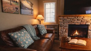 A cozy living room with a stone fireplace, leather sofa, and a table with a book and mug.