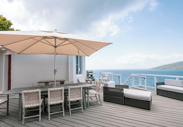 A deck with a table and chairs, a large umbrella, and a view of the sea. - Unrivaled Oceanfront Views In Our Private Caribbean Resort (St Thomas)