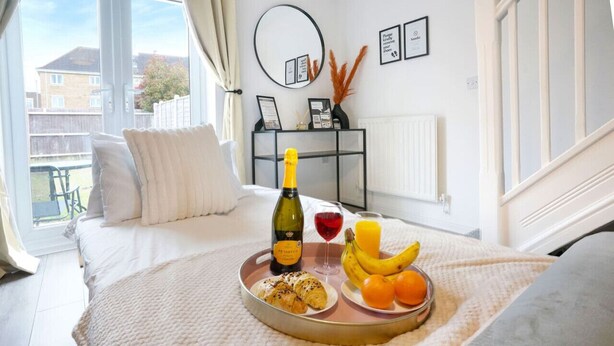 A bedroom with a bed, a tray with croissants, a bottle of wine, and fruit. - Welcoming House with Free Parking and Fast WiFi (Luton)