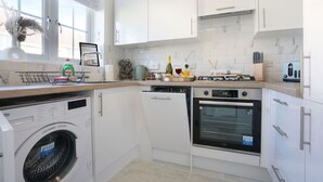 A modern kitchen with white cabinetry, a built-in washing machine, an oven, and a window with a view. - Welcoming House with Free Parking and Fast WiFi (Luton)