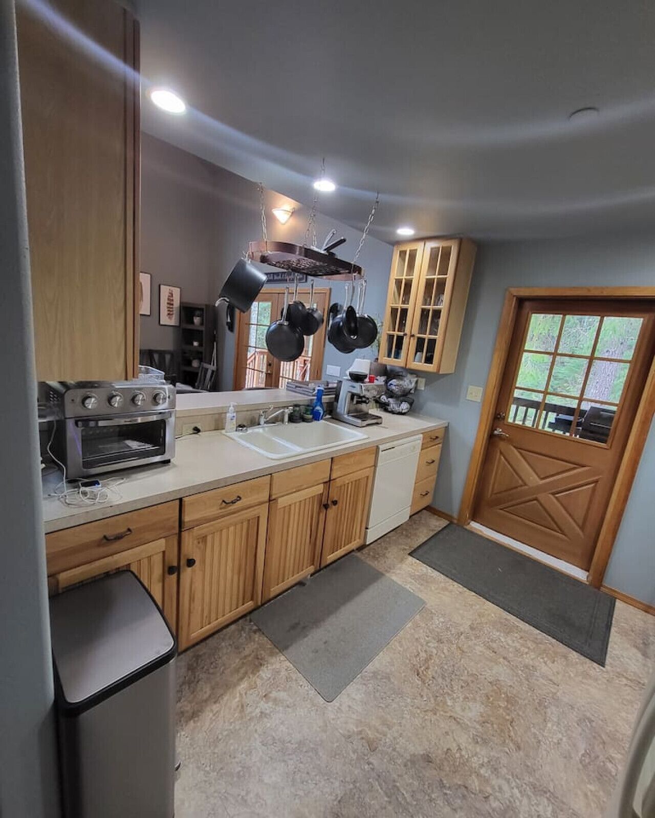 A kitchen with wooden cabinets, a built-in oven, a sink, and hanging pots.