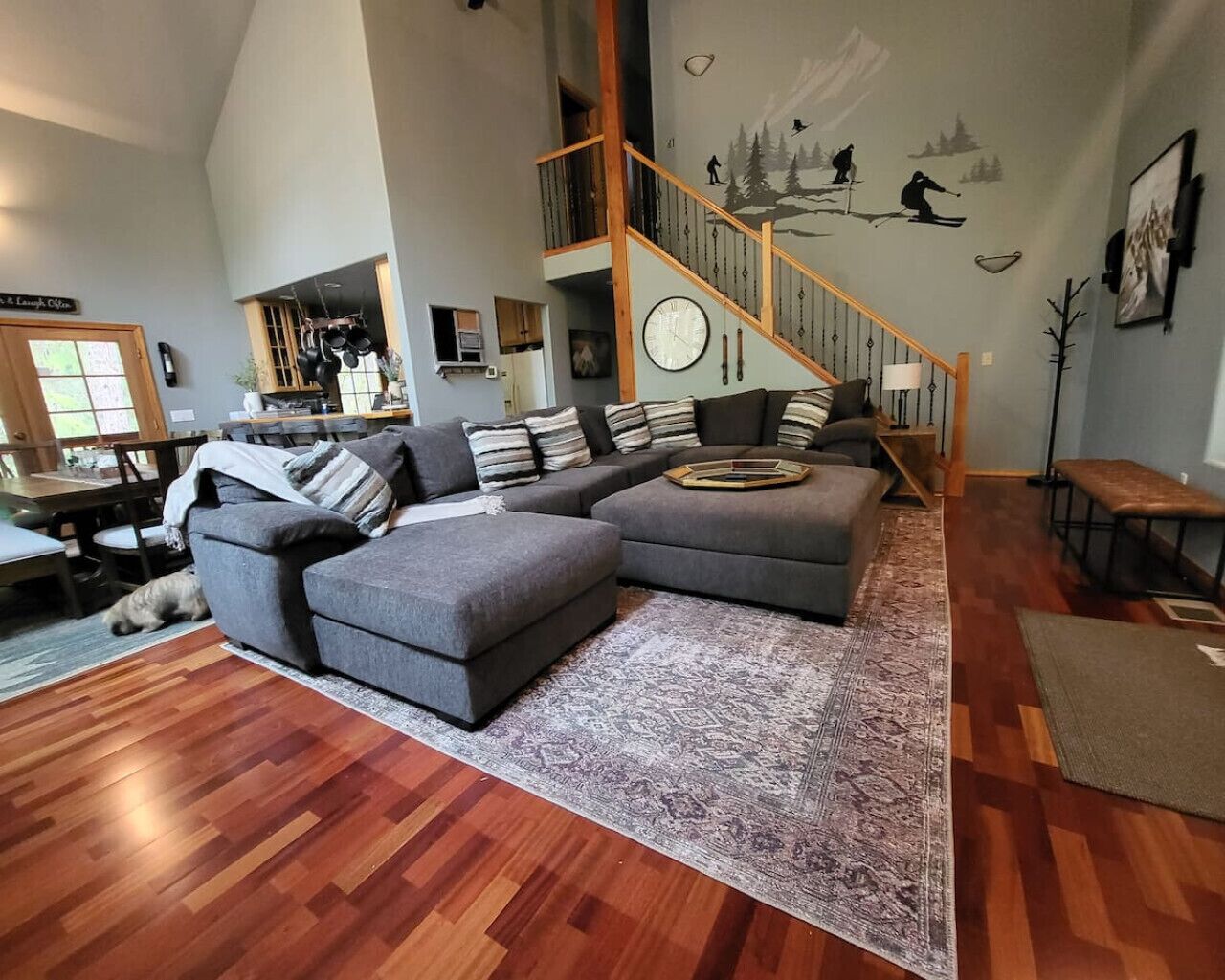 Un salon spacieux avec un grand canapé d’angle, un escalier en bois et un coin repas.