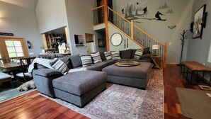 Un salón amplio con un sofá seccional grande, una escalera de madera y un comedor.