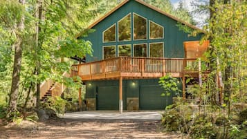 A two-story wooden cabin with a balcony, surrounded by dense forest.
