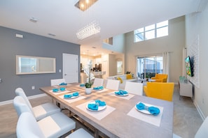 Uma área de refeições moderna, com uma mesa comprida, cadeiras brancas e guardanapos azuis.