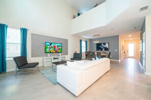 Ein modernes Wohnzimmer mit einem weißen Sofa, einem Flachbildfernseher und einem Essbereich mit Stühlen und einem Tisch.