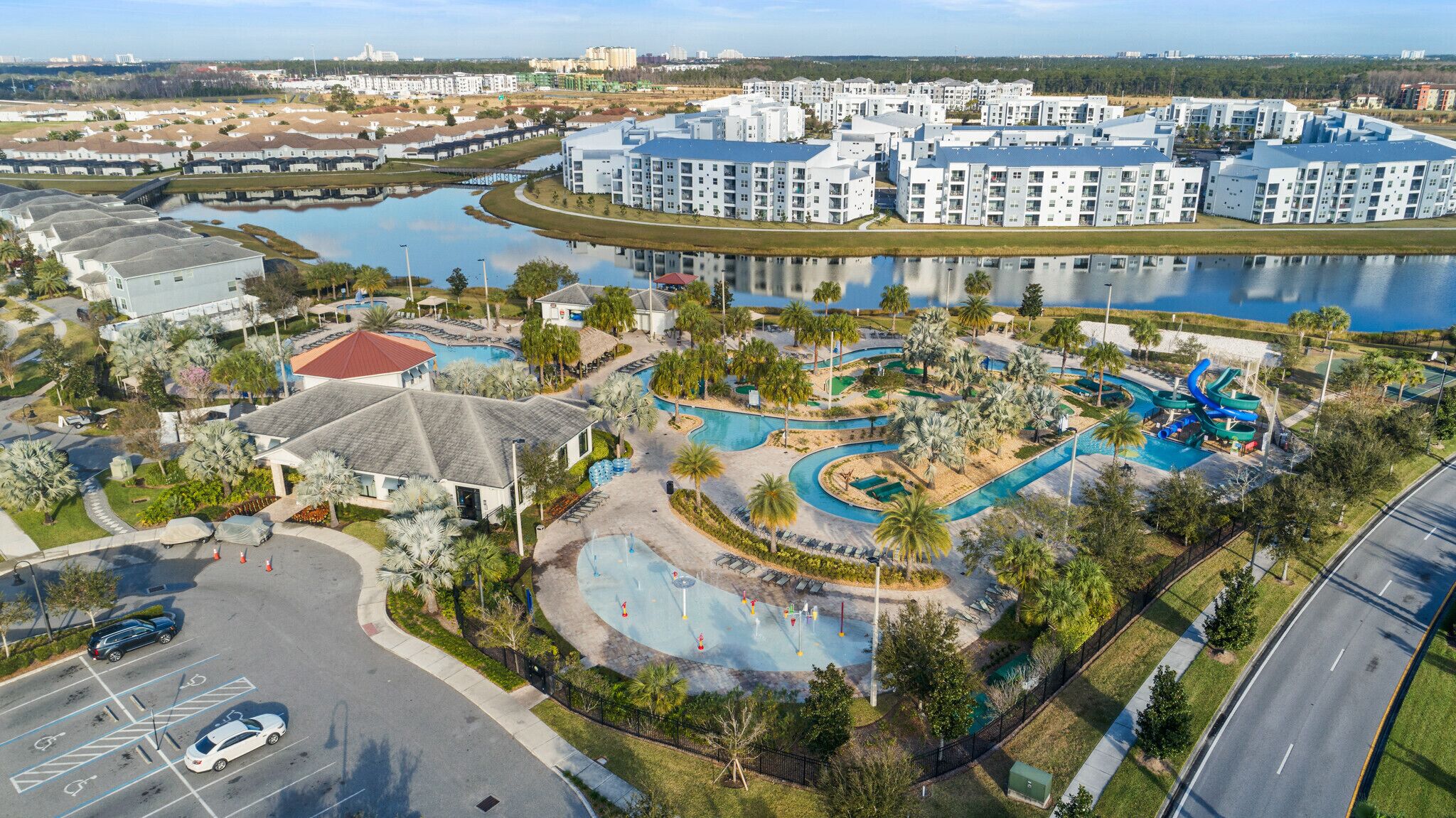 A residential area with modern apartment buildings, a swimming pool complex, and a road with a pedestrian walkway.