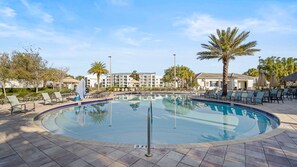 A circular pool with lounge chairs and palm trees, surrounded by a building with multiple floors. - Awesome Villa 5Beds/5Bath/Pool/Jacuzzi/5Min From Disney (Kissimmee)