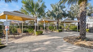 A covered outdoor seating area with chairs and tables, surrounded by palm trees and a paved walkway. - Awesome Villa 5Beds/5Bath/Pool/Jacuzzi/5Min From Disney (Kissimmee)