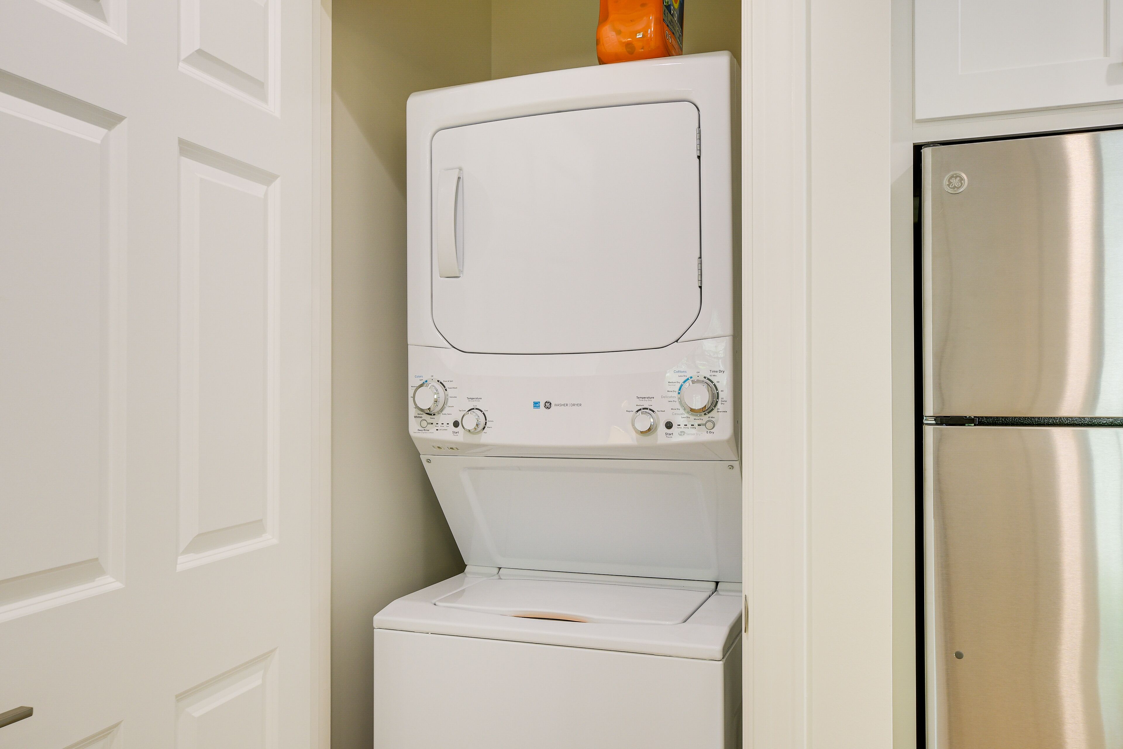 Un appareil combiné lave-linge et sèche-linge, de dimensions réduites, installé dans une cuisine dotée de meubles blancs et d’un réfrigérateur en acier inoxydable.