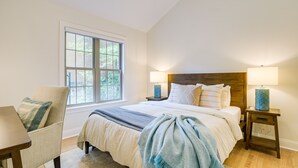 Ein Schlafzimmer mit einem großen Bett, zwei Nachttischen, einem Sessel und einem Fenster.