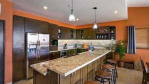 Cozinha moderna com ilha central, armários escuros e geladeira de aço inoxidável.