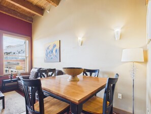 A dining area with a wooden table, chairs, and a bowl centerpiece. There is a painting on the wall and a lamp on the side. - High Ceilings with Loft and Private Patio (Victoria)
