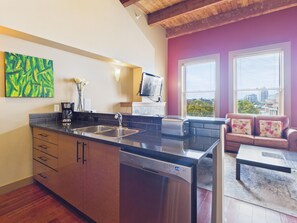 A modern kitchen with a dishwasher, a coffee maker, and a toaster. There is a dining area with a sofa and a coffee table.