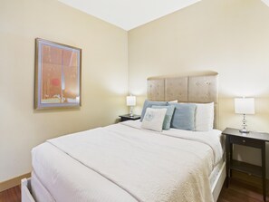 A hotel room with a large bed, a headboard, two bedside tables, and a wall-mounted picture.