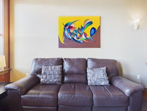 A brown leather sofa with two cushions against a wall with a colorful abstract painting.