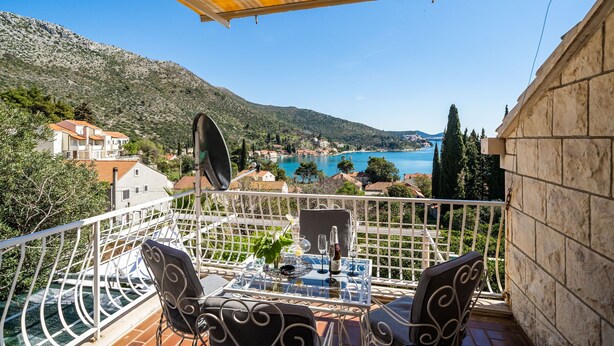 A balcony with a table, chairs, and a view of a lake and mountains.