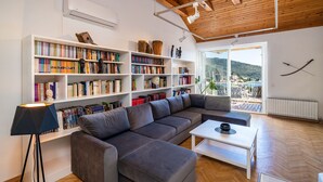 A modern living room with a large sectional sofa, a white coffee table, and a floor lamp. There are multiple bookshelves filled with books and decorative items.