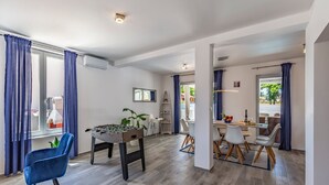 Un vaste espace de vie comprenant un baby-foot, une table à manger avec des chaises et un coin cuisine visible à travers une porte ouverte.