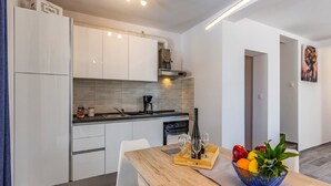 Une cuisine moderne avec des meubles blancs, une table à manger en bois et un panier de fruits.