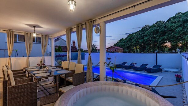 Une terrasse sur le toit avec un jacuzzi, un espace salon et une vue sur une piscine et des arbres.