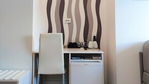 A small, modern office space with a white desk, two chairs, a white filing cabinet, and a wall-mounted shelf with office supplies.