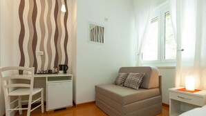 A small, well-lit room with a bed, a desk, and a chair.