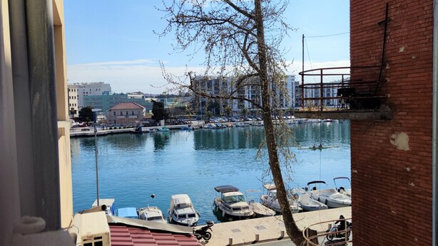 A marina with boats docked, a clear sky, and buildings in the background.