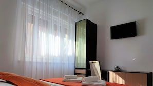 A hotel room with a bed, a desk, a mirror, and a TV on the wall.