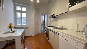 A modern kitchen with white cabinetry, a stainless steel sink, and a dishwasher. There is a window with multiple panes and a vase with flowers on the counter.