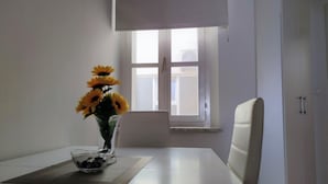 A room with a white table, a vase with sunflowers, a bowl, and a window with blinds.