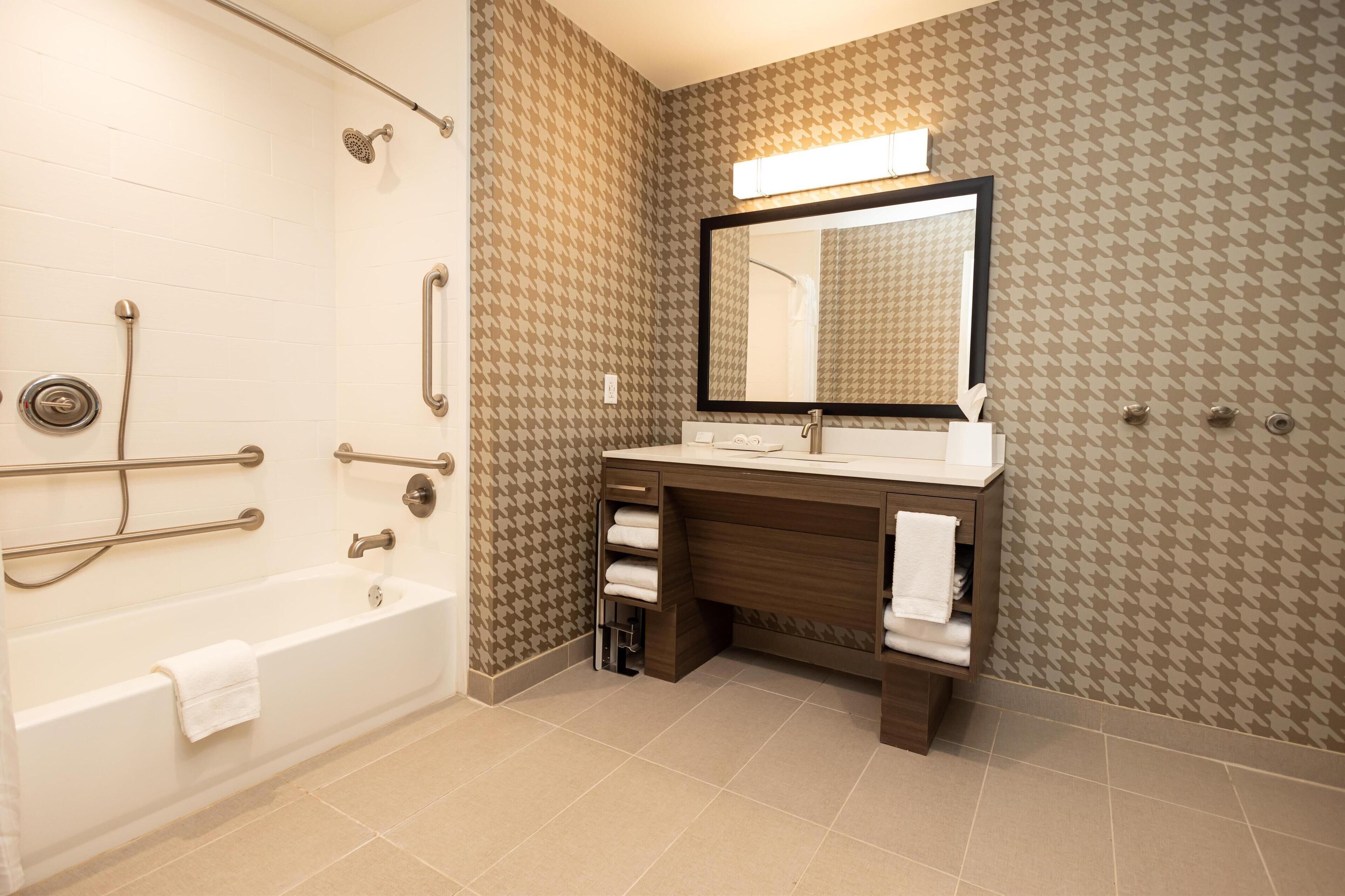 A bathroom with a bathtub, a vanity with a mirror, and a towel rack.