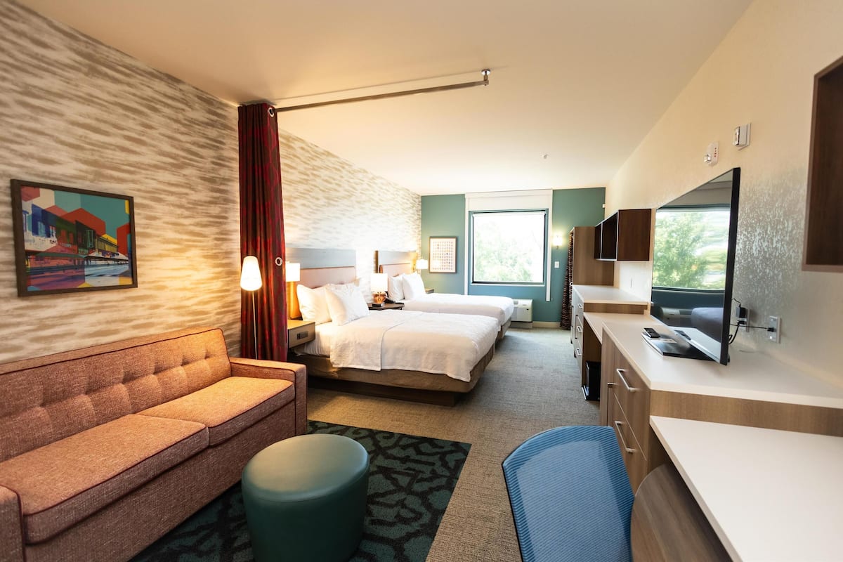 A hotel room with a sofa, two beds, a desk, and a TV.