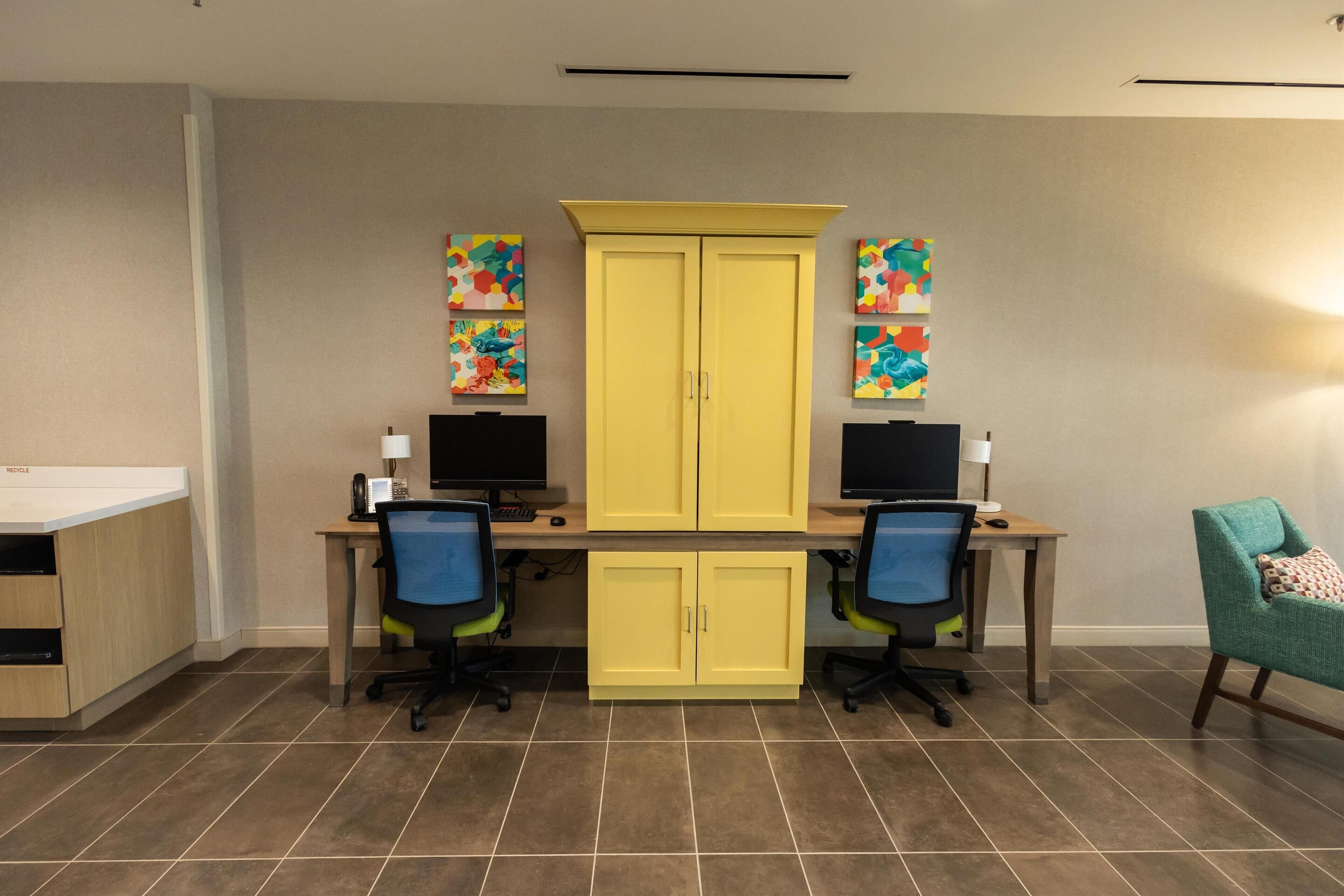 A room with two desks, two chairs, a yellow cabinet, and artwork on the walls.