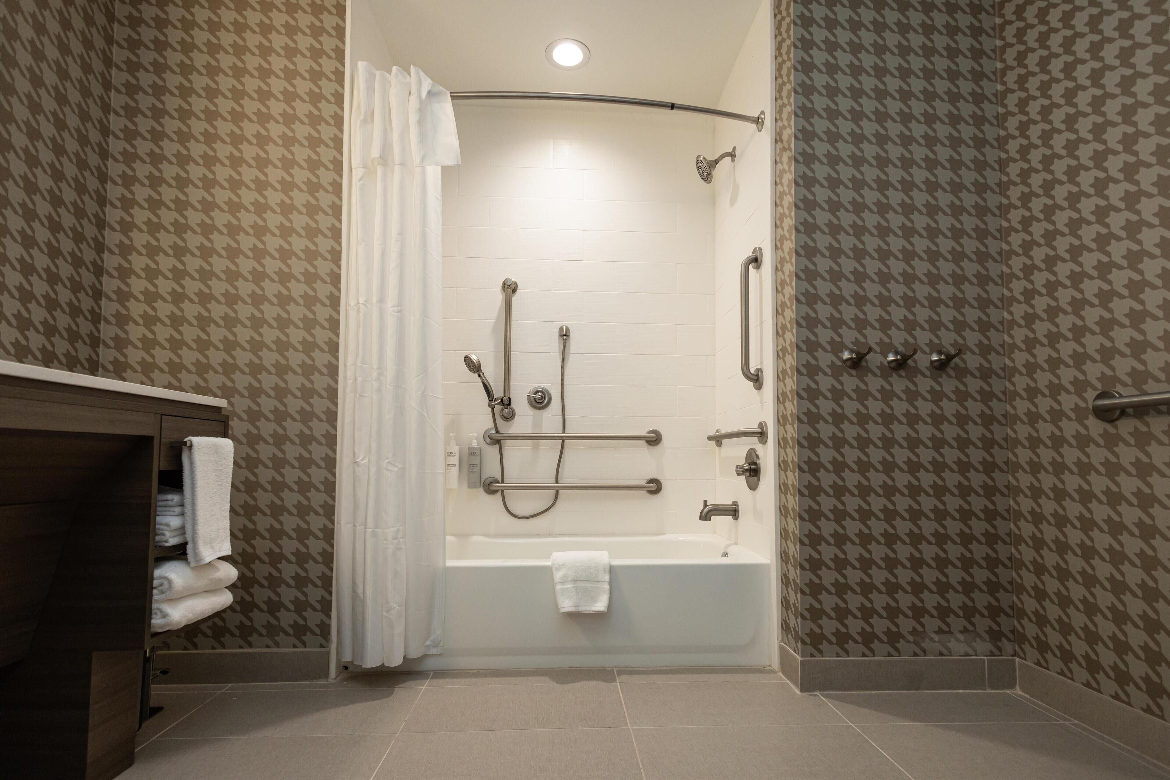 A modern bathroom with a walk-in shower, grab bars, and a towel rack.