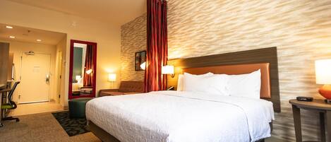 Ein Hotelzimmer mit einem großen Bett, einem Schreibtisch, einem Sessel und einem Spiegel.