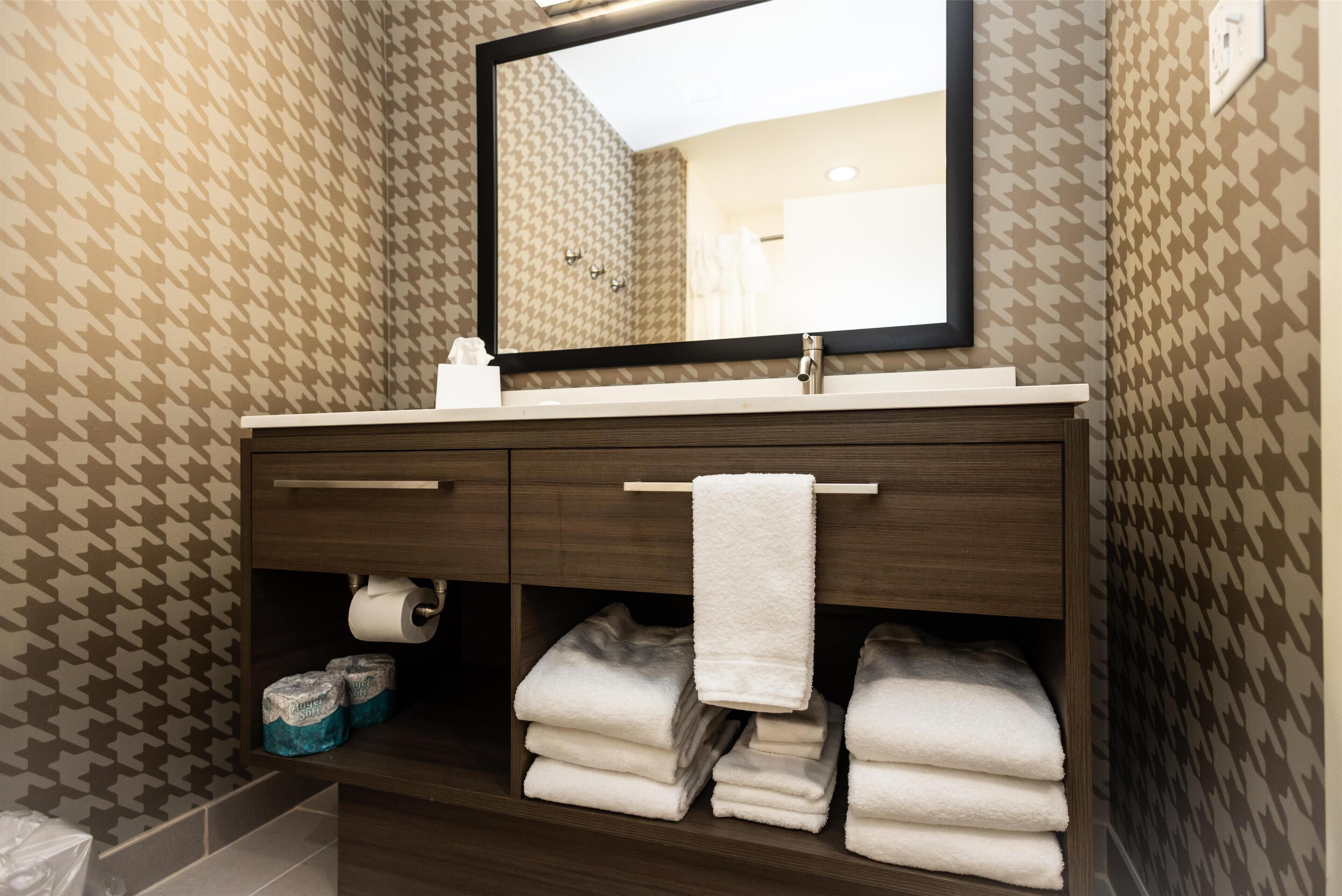 Une salle de bain avec un papier peint à motifs, un miroir, un lavabo et des serviettes soigneusement pliées.