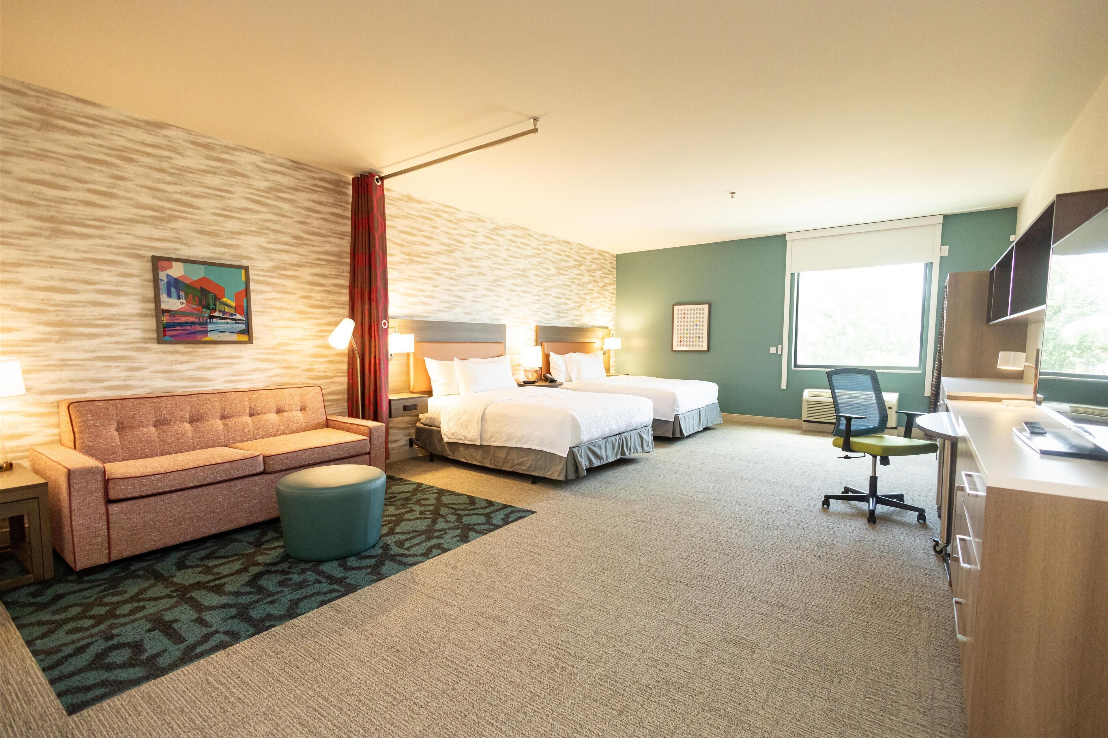A hotel room with two beds, a sofa, a desk, and a TV.