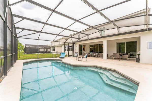 Un espace piscine extérieur abrité, doté d'un toit en verre, de chaises longues et d'un barbecue.
