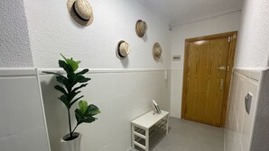 A hallway with a white wall, a wooden door, a small white table with a mirror, and a potted plant. - Ruim Modern Familie Appartement in Torrevieja Spanje (Torrevieja)