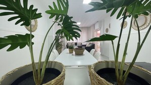 A dining area with a white table, white chairs, and large potted plants with broad leaves. - Ruim Modern Familie Appartement in Torrevieja Spanje (Torrevieja)