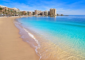 Una spiaggia con acque cristalline turchesi, una riva sabbiosa e una fila di edifici sullo sfondo.