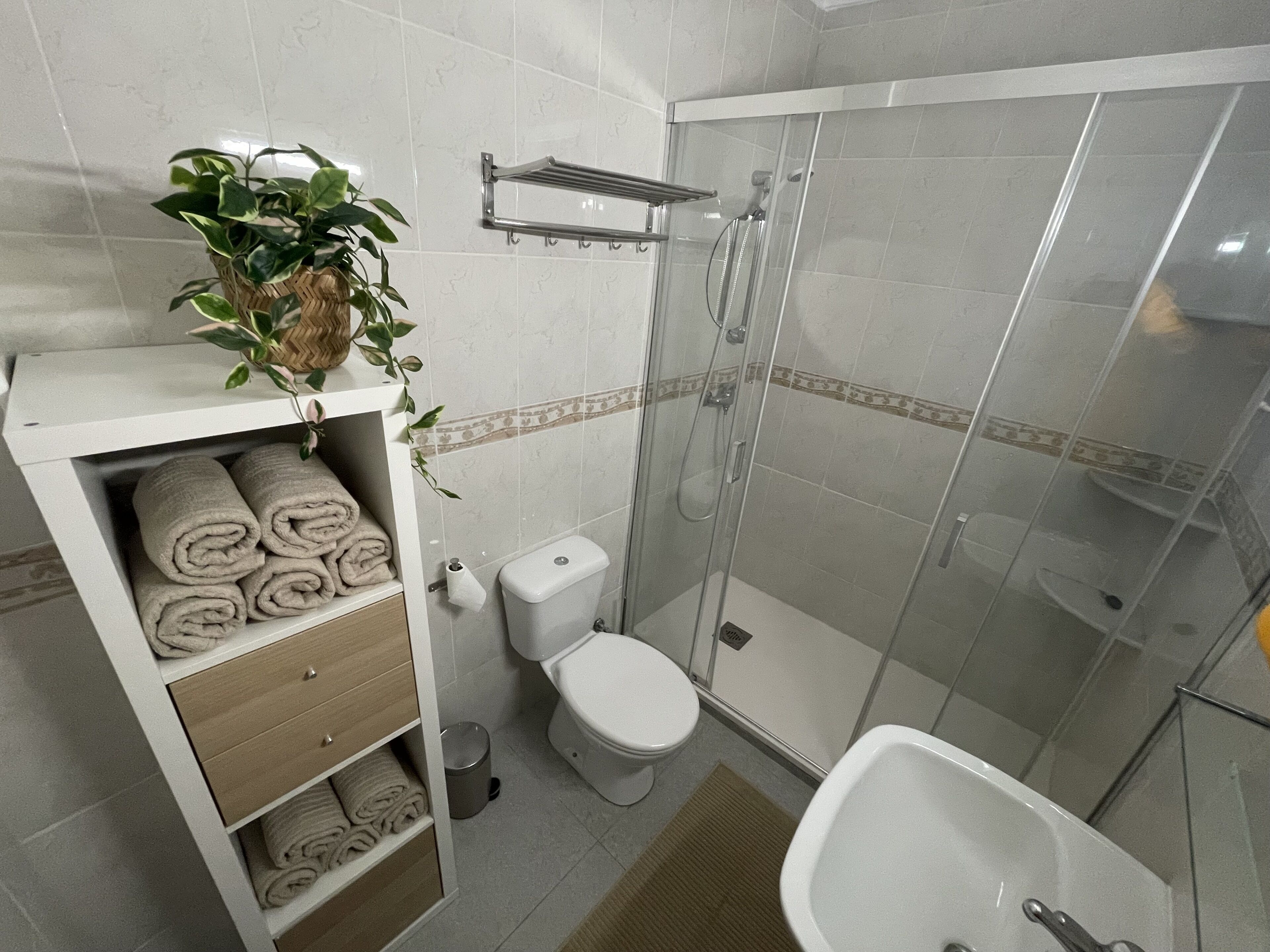 Ein Badezimmer mit Toilette, Duschkabine, Waschbecken und einem Regal mit Handtüchern.