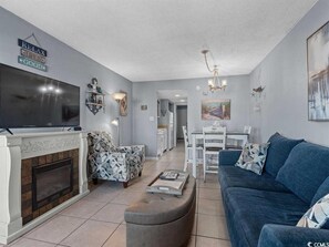 Una sala de estar moderna con chimenea, un sofá azul y un comedor con mesa y sillas blancas.