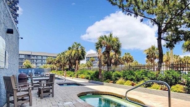 A pool area with a small pool, lounge chairs, and a wooden table.
