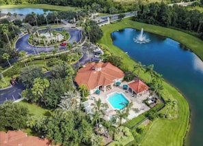 An aerial view of a resort with a swimming pool, a fountain, and a road network.