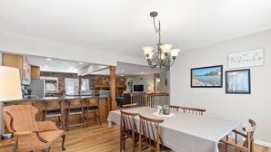 Un vaste espace de salle à manger avec une longue table et des chaises en bois, une cuisine avec un pare-feu en pierre et un lustre.