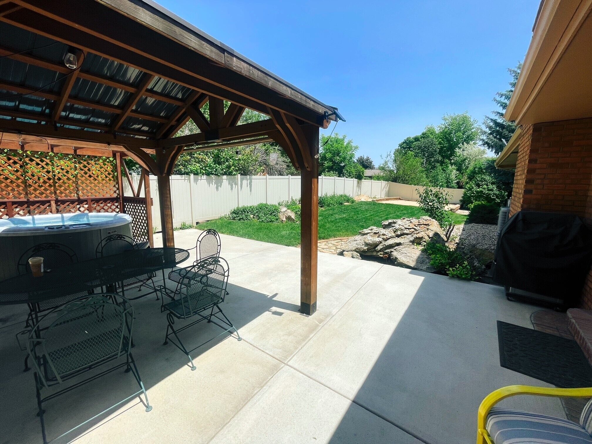 A covered patio area with a hot tub, grill, and outdoor seating.